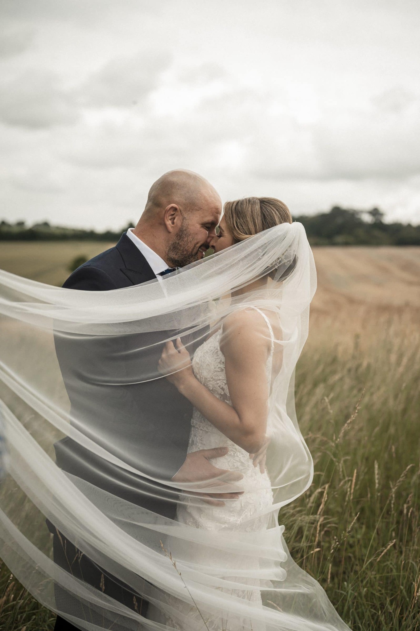 Newlyweds embraced beneath a flowing veil in an Irish field