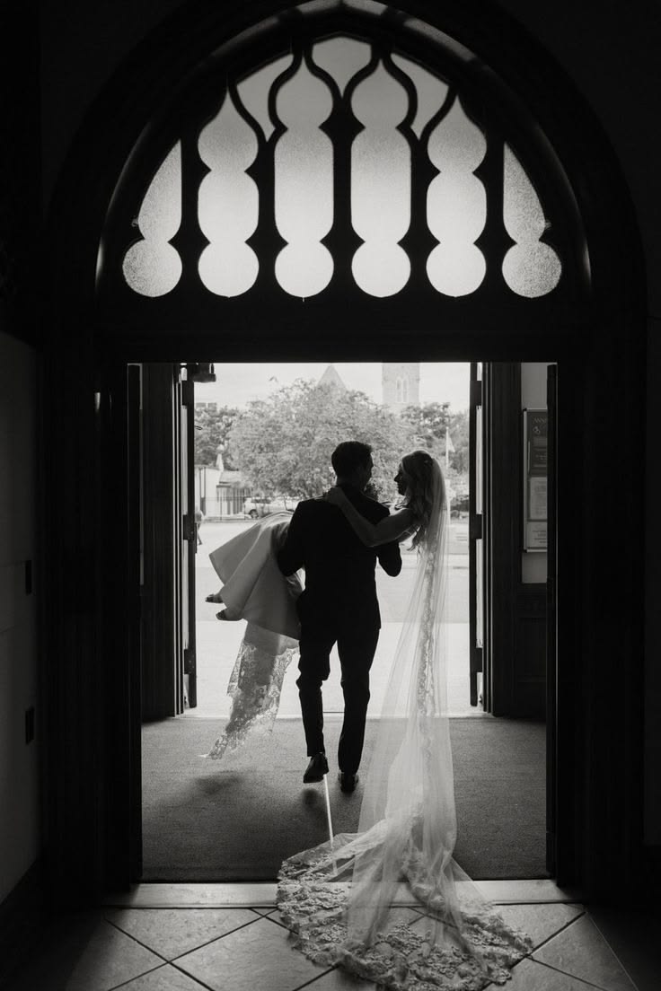 Groom carrying the bride through a church doorway in black and white
