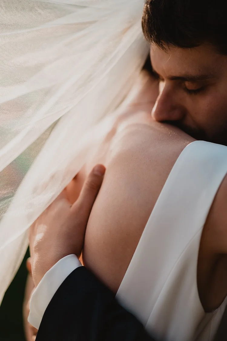 Groom kissing the bride beneath her veil in warm natural light