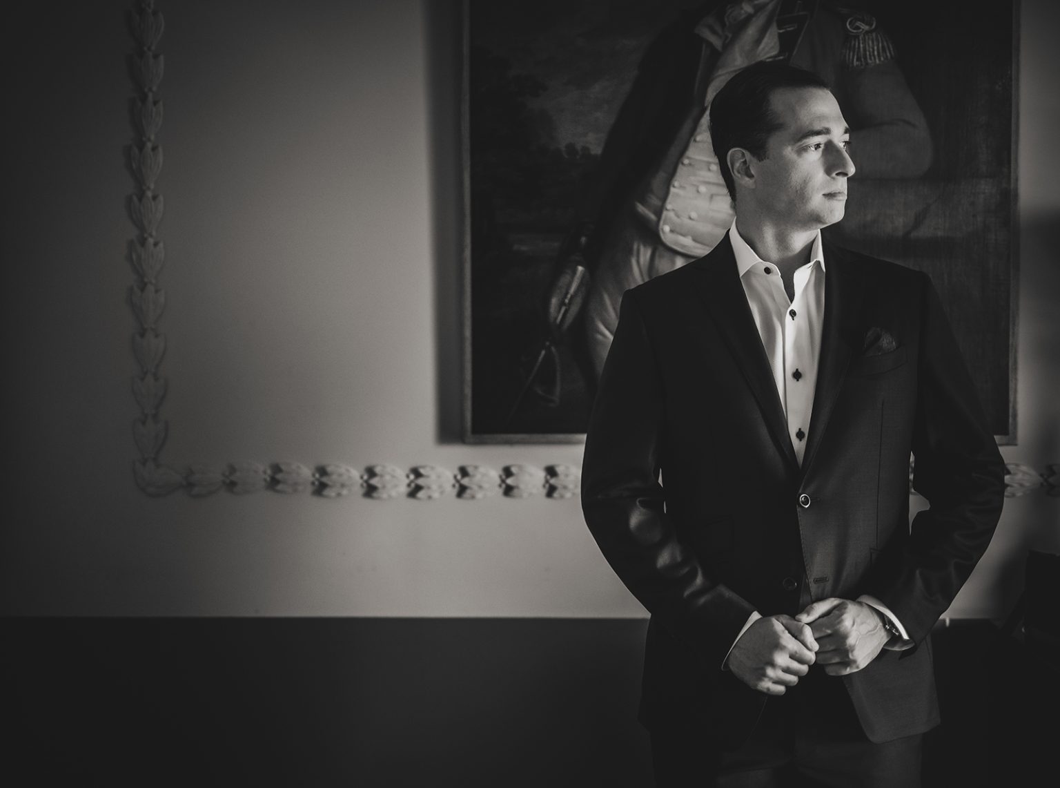 Black and white portrait of a groom standing by window light