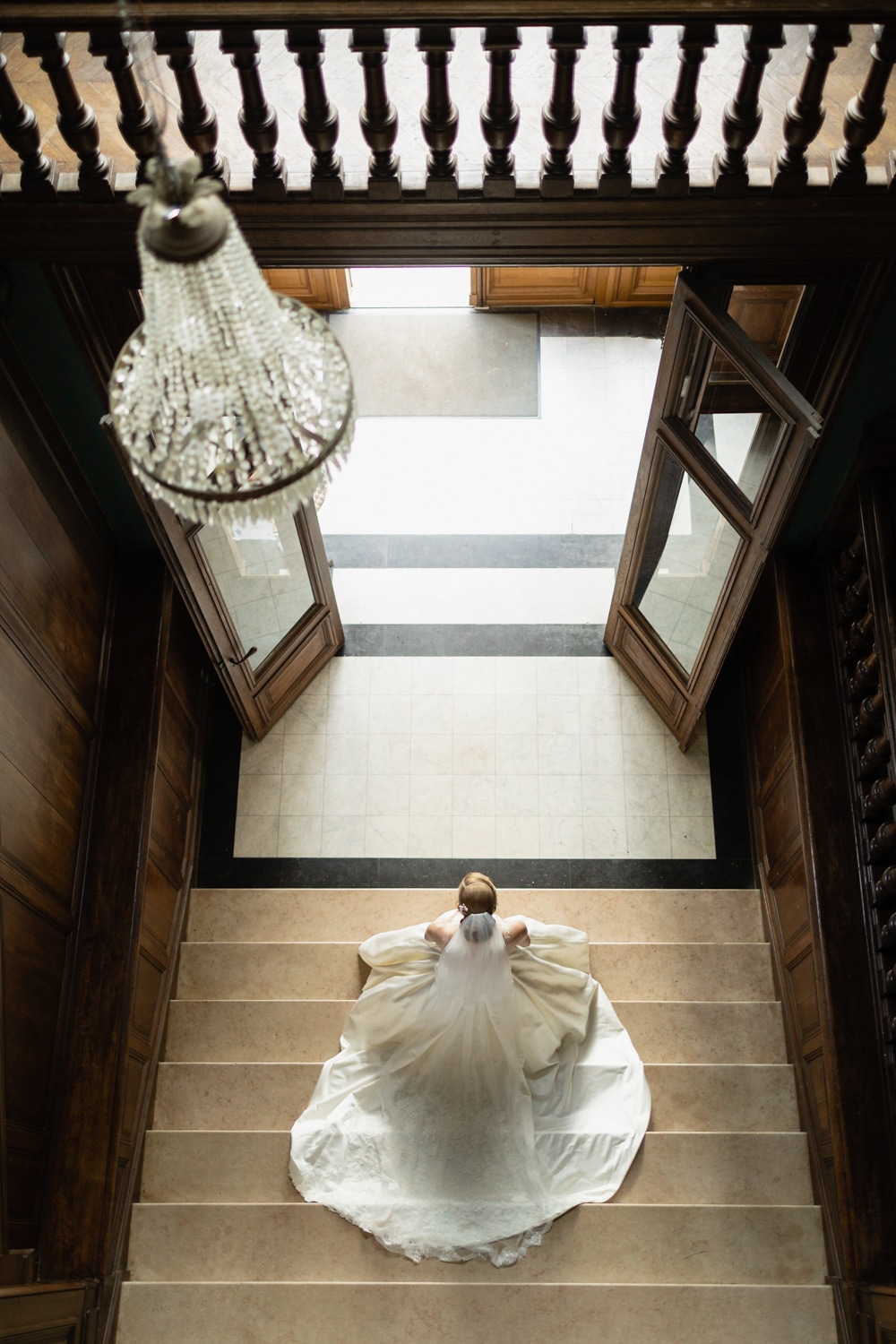 Bride seen from above sitting on a grand staircase in an elegant venue
