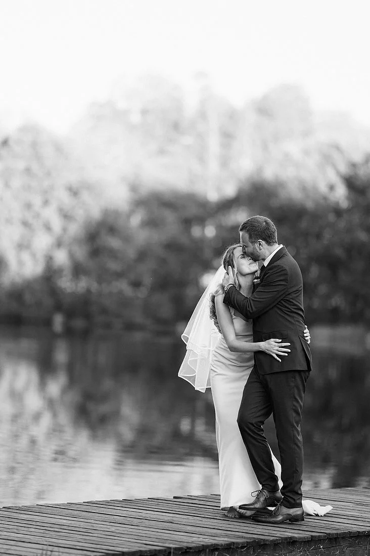 Newlyweds sharing a kiss beside a lake in black and white
