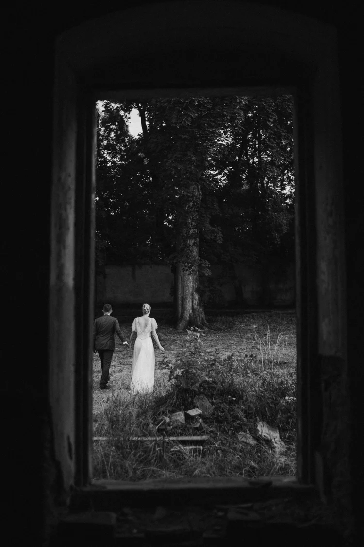 Black and white view of newlyweds walking outdoors through a dark window frame