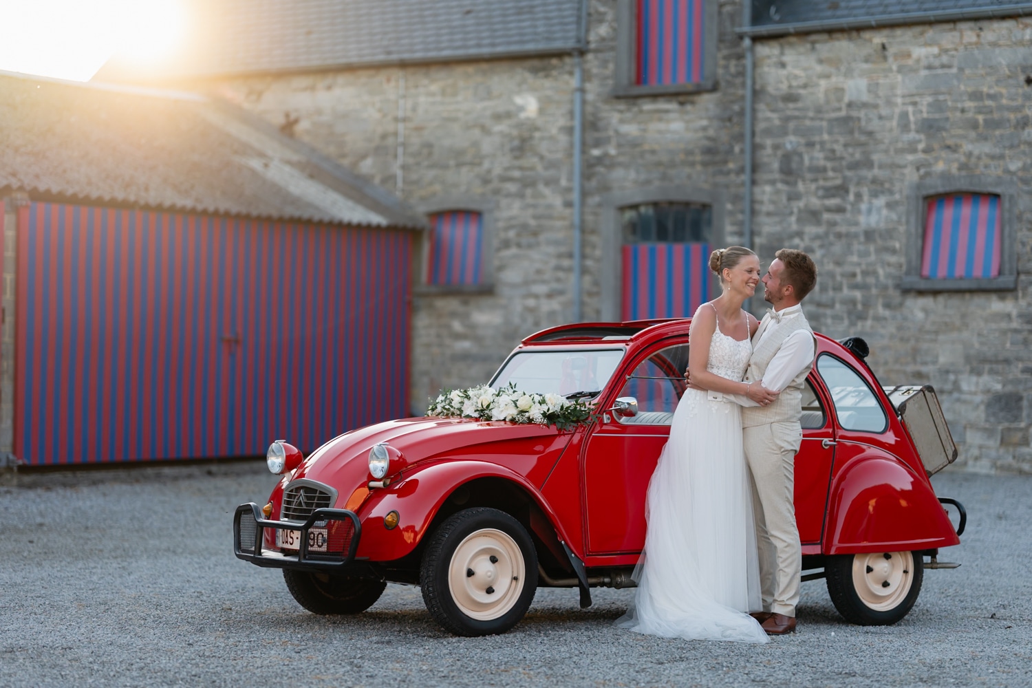 Newlyweds kissing beside a classic car