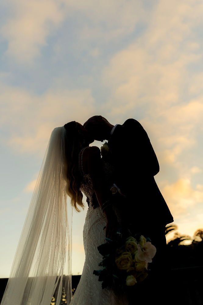Newlyweds kissing in silhouette beneath a warm sunset sky