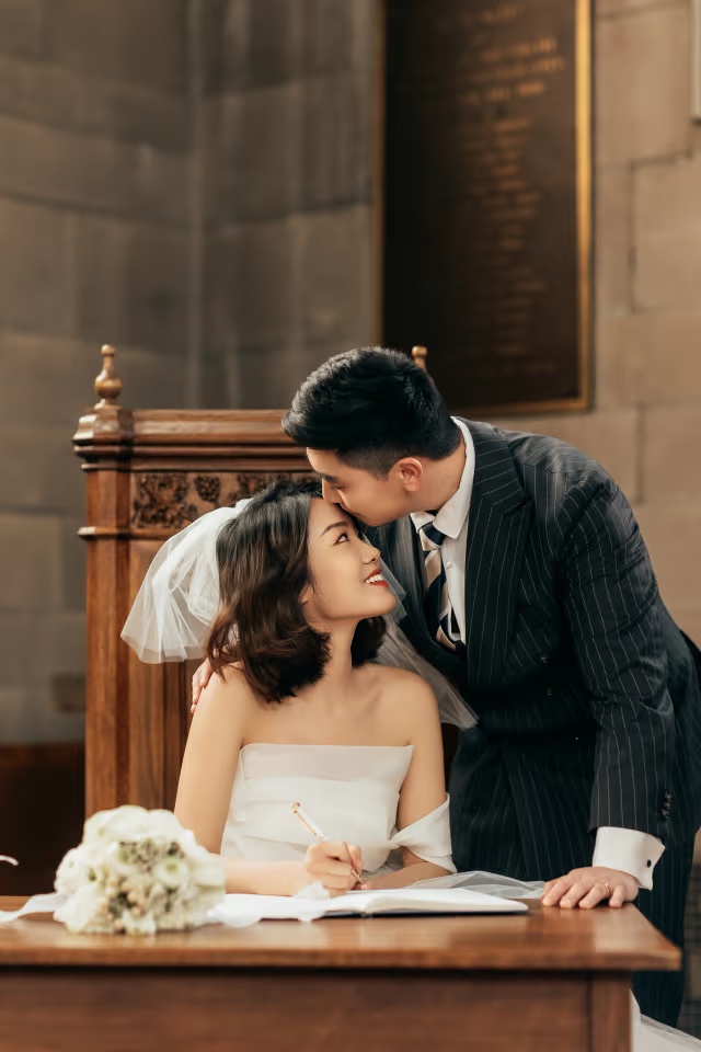 Groom kissing the bride while she signs the wedding register